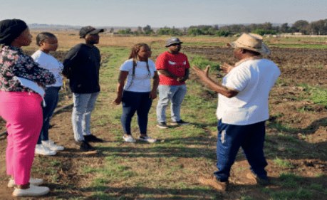 A group of TVET students listening to a farm supervisor in a field